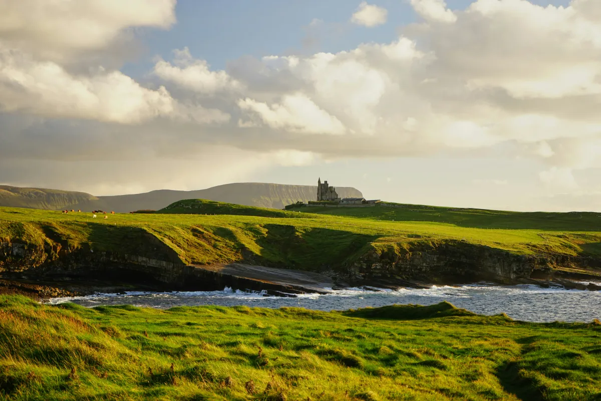 Üppige Küstenlandschaft in Irland mit Burg im Hintergrund