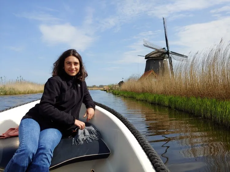 Junge Frau sitzt auf kleines Motorboot und fährt an Mühle vorbei in der Niederlande