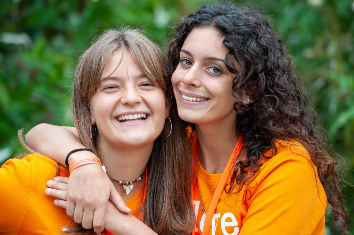 Zwei Schülerinnen halten sich lachend in orangen T-Shirts