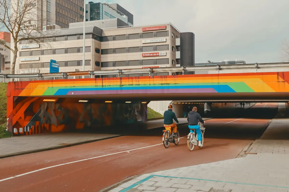 Fahrradweg mit zwei Fahrradfahrer unter Brücke mit Pridefarben