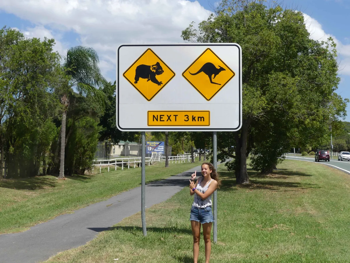 Mädchen steht unter Strassenschild Achtung Wildtiere in Australien