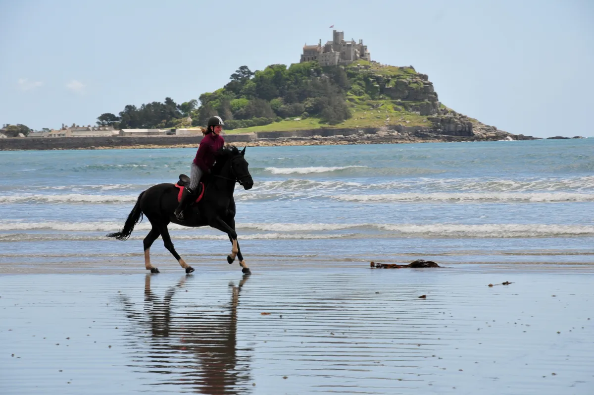 Reiterin galoppiert am Strand vor englischer Insel mit Schloss drauf
