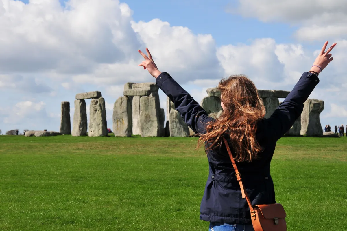 Mädchen streckt Arme hoch mit Peace-Fingern vor Stonehenge