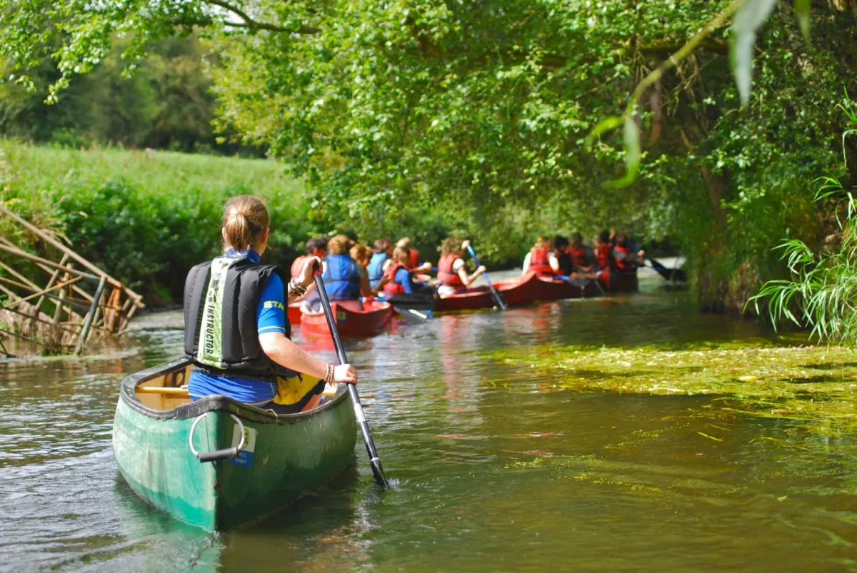 Gruppe auf Kanufahrt auf grünem Fluss unter Bäumen