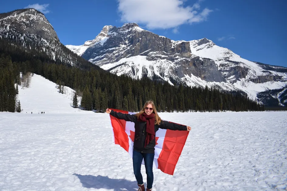 Schülerin steht auf schneebedecktem See mit Kanadischer Flagge bei blauem Himmel