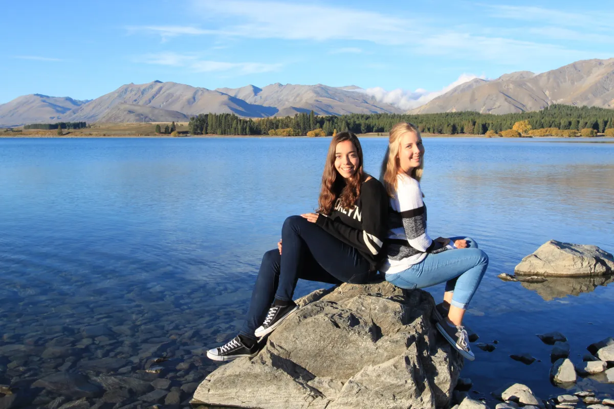 Zwei Mädchen sitzen auf Stein an grossem See in Neuseeland