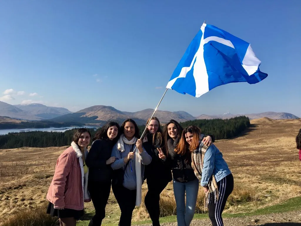 Schüler mit schottischer Flagge im Hochland vor Hügel und Wiesen