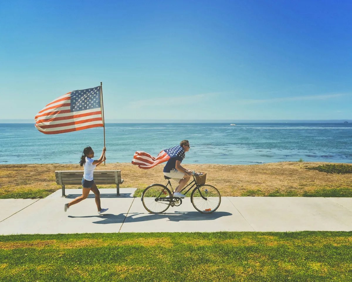 Zwei Velofahrer mit USA Flaggen radeln entlang vom Meer
