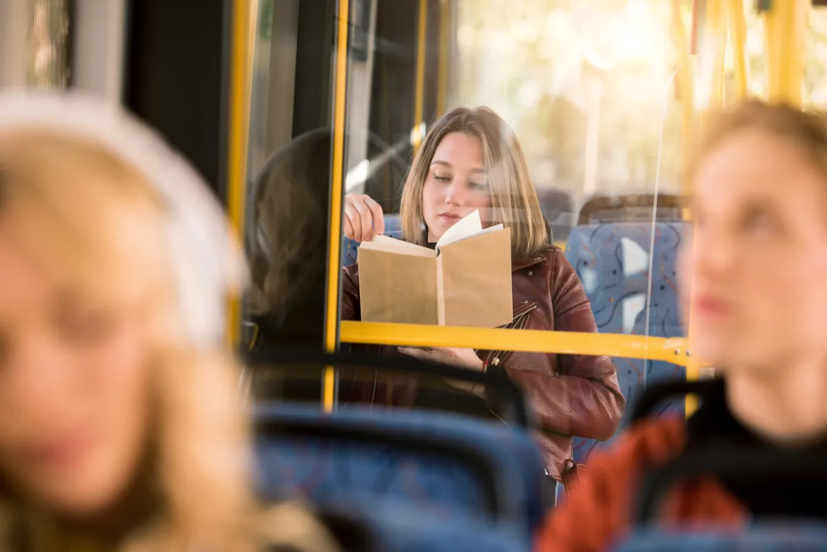 Schülerin sitzt im Bus und liest ein Buch. 