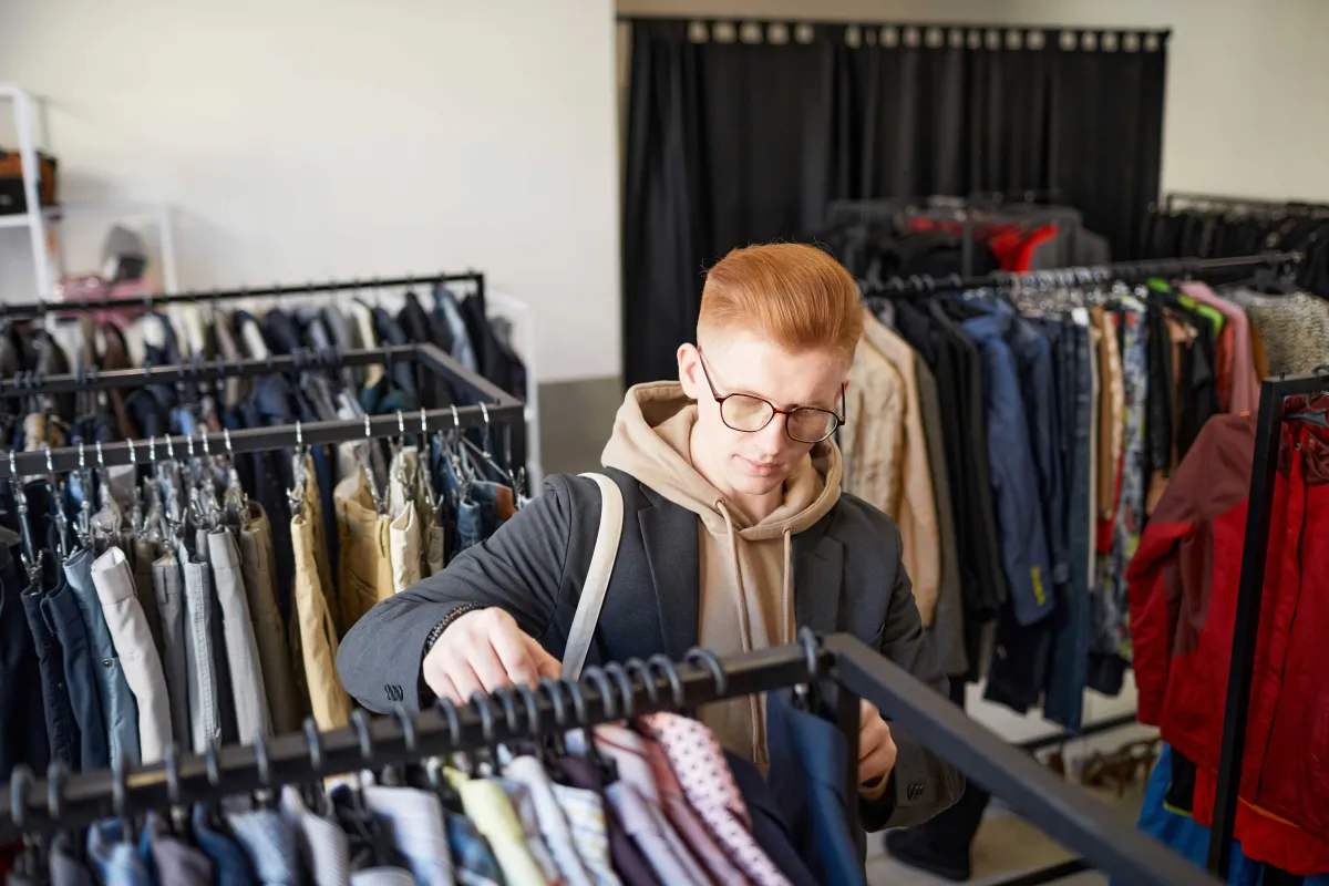 Schüler kauft in Secondhand Kleider laden ein, sucht ein Hemd aus
