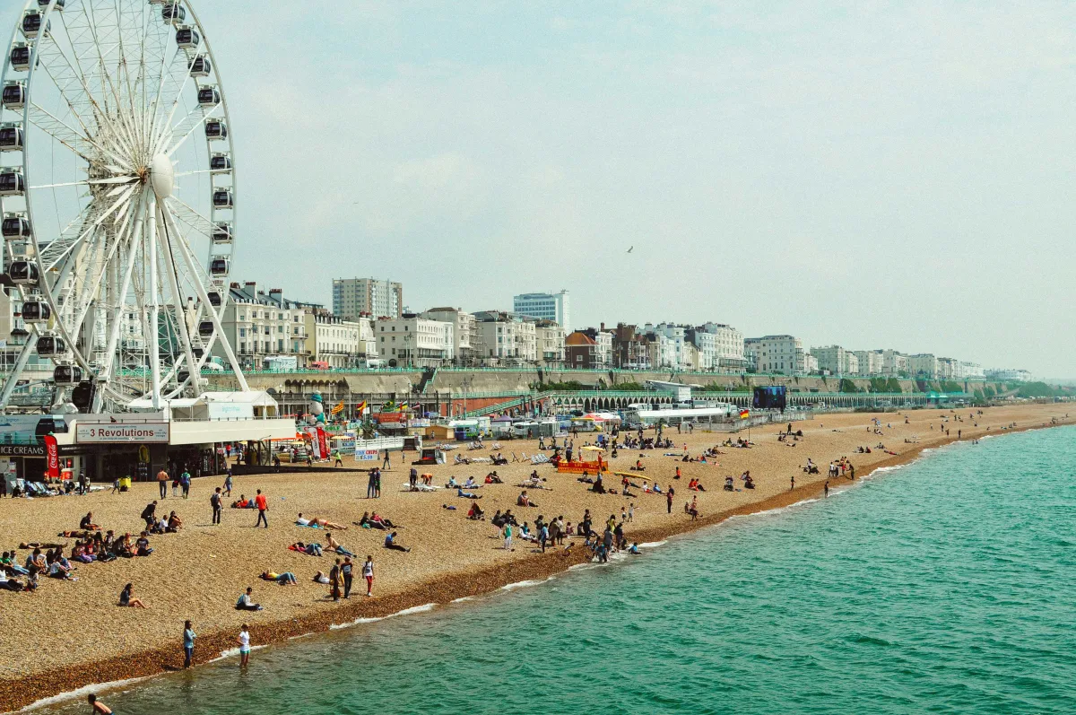 Sommertag in Brighton, England am Strand. Riesenrad im Hintergrund, blaues Meer und viele Leute am Strand