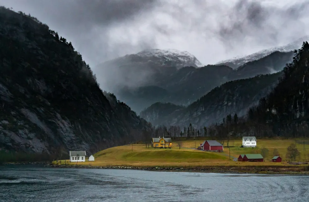 Siedlung in dunkler Bucht in Norwegen in Abenddämmerung mit grünen Feldern und das Meer im Vordergrund.