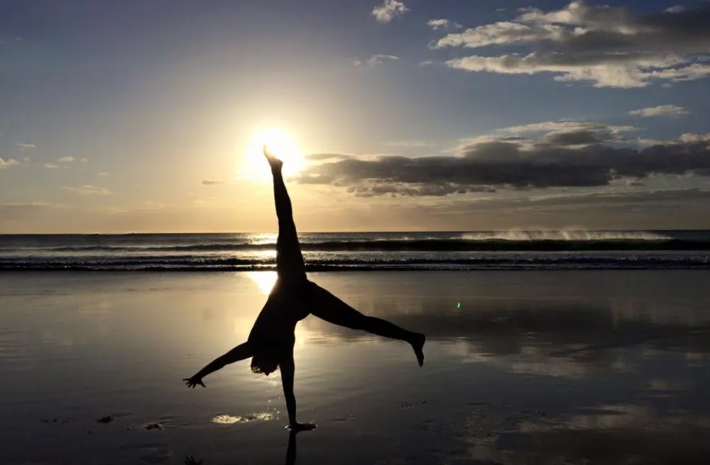 Mädchen macht Handstand am Strand während Sonnenuntergang