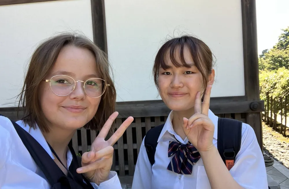 Austauschschülerin mit japanischer Schülerin lachendes Peace Selfie in Schuluniform