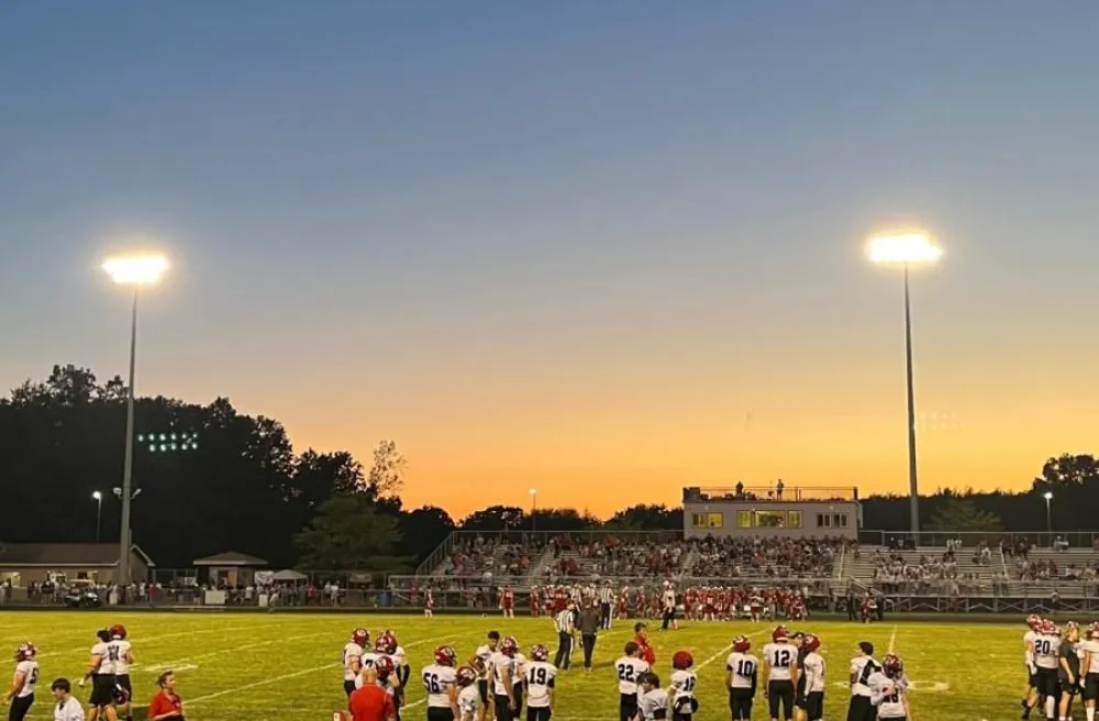 Footballspiel bei Sonnenuntergang mit Cheerleadern und Zuschauenden auf den Tribünen.