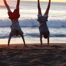 Zwei Jungen machen Handstand am Strand mit Sonnenuntergang im Hintergrund
