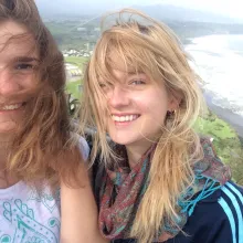Zwei junge blonde Frauen mit Haar im Gesicht wegen Wind an Küste neben Meer