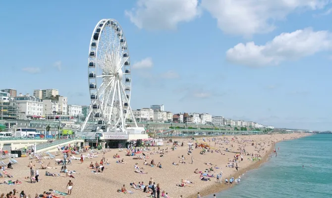 Riesenrad an der Südküste Englands am Strand mit vielen Menschen bei Sonnenschein
