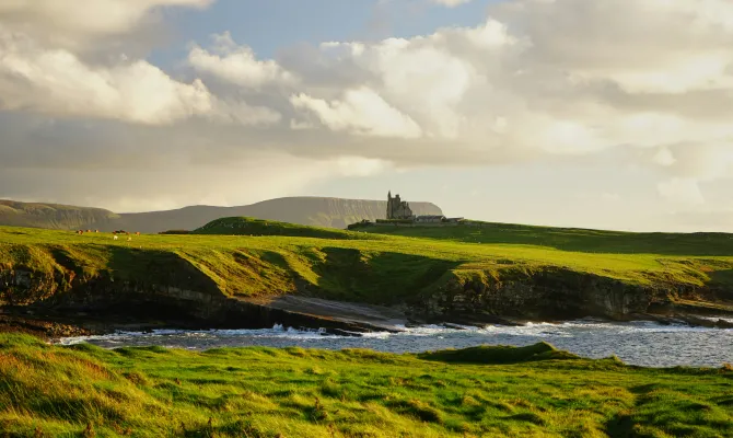 Üppige Küstenlandschaft in Irland mit Burg im Hintergrund