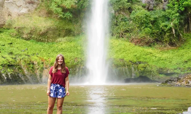 Austauschschülerin steht unter hohem Wasserfall in Neuseeland.