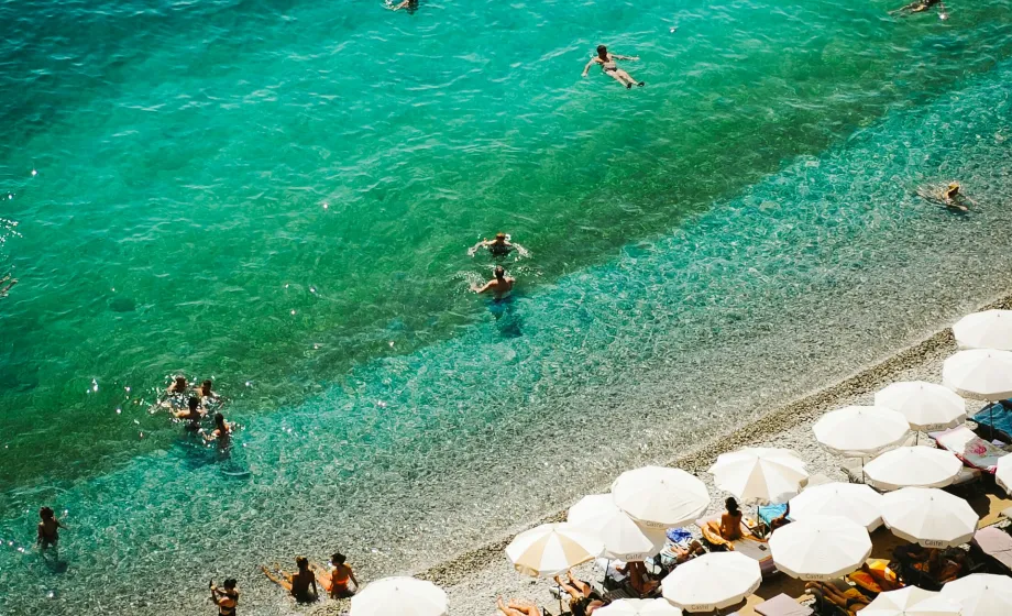 Türkisfarbenes Meer mit Strand und weissen Sonnenschirmen
