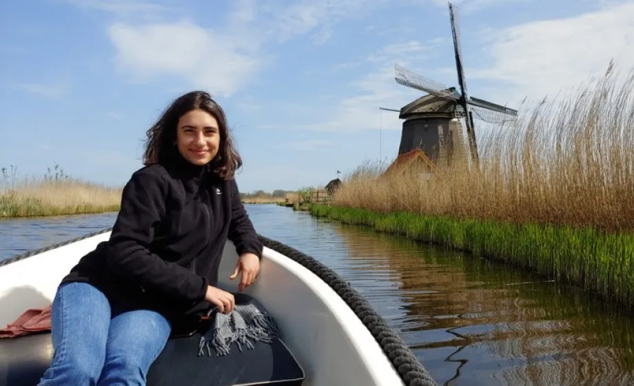 Junge Frau sitzt auf kleines Motorboot und fährt an Mühle vorbei in der Niederlande