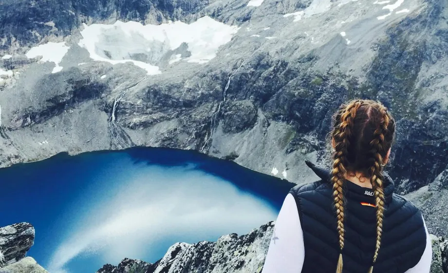 Mädchen von hinten schaut über tiefen Fjord mit Gletscher und grauen Felswänden