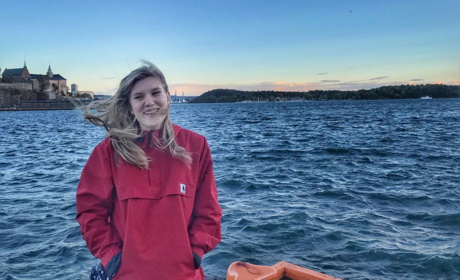 Schülerin in roter Jacke auf Boot lächelt vor dunkelblauem Wasser