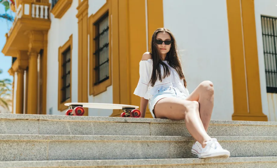 Junge Frau sitzt auf Steintreppe in sommerlichem, weissen Kleid mit Sonnenbrille