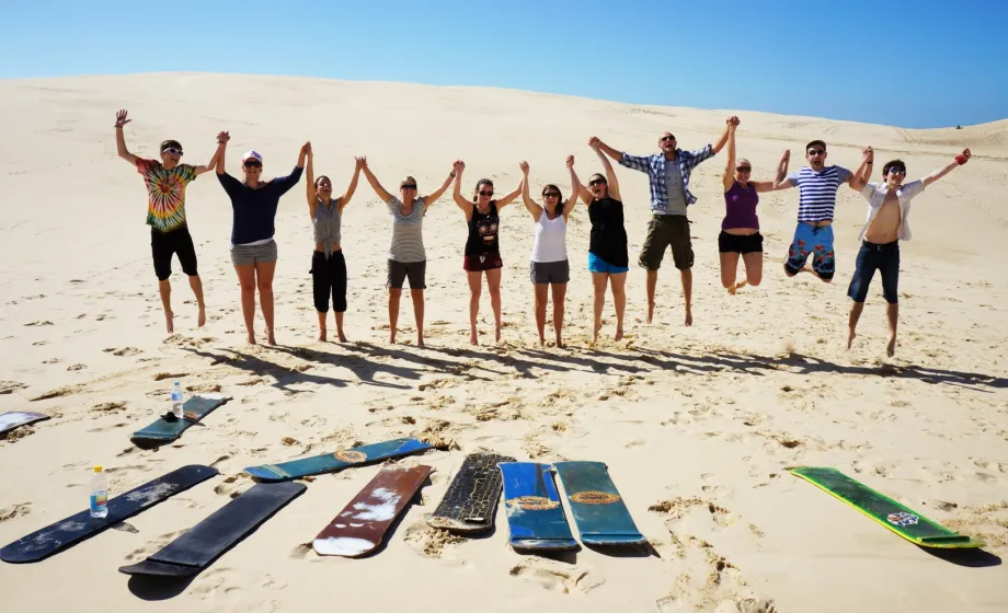 Gruppe junge Menschen springend in weisser Wüste mit blauem Himmel und Sandboards