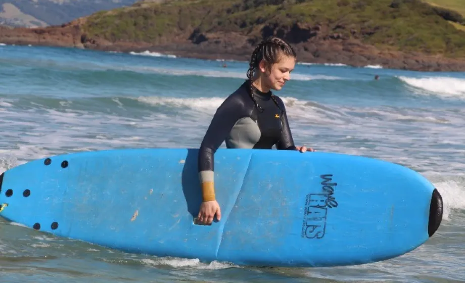 Suferin mit blauem Surfboard läuft aus Wasser lachend