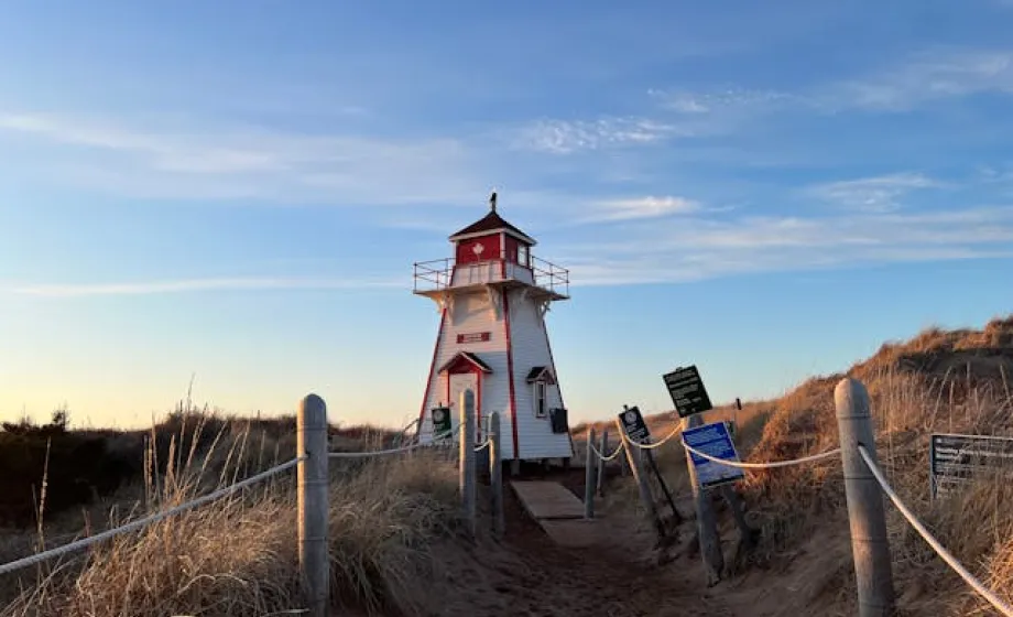 Morgendämmerung bei rot-weissem Leuchtturm zwischen braunen Feldern und blauem Himmel