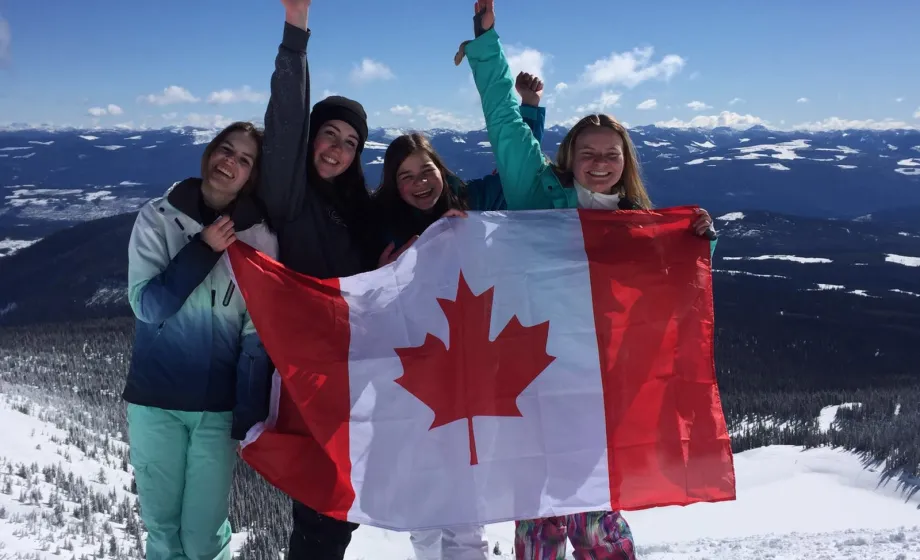 Vier Schülerinnen stehen in Winterlandschaft mit kanadischer Flagge jubelnd