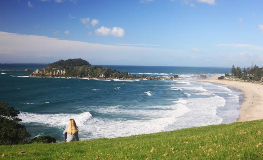 Strand mit weissen Wellen und grüne Wiese davor und sitzendes Mädchen in Wieser
