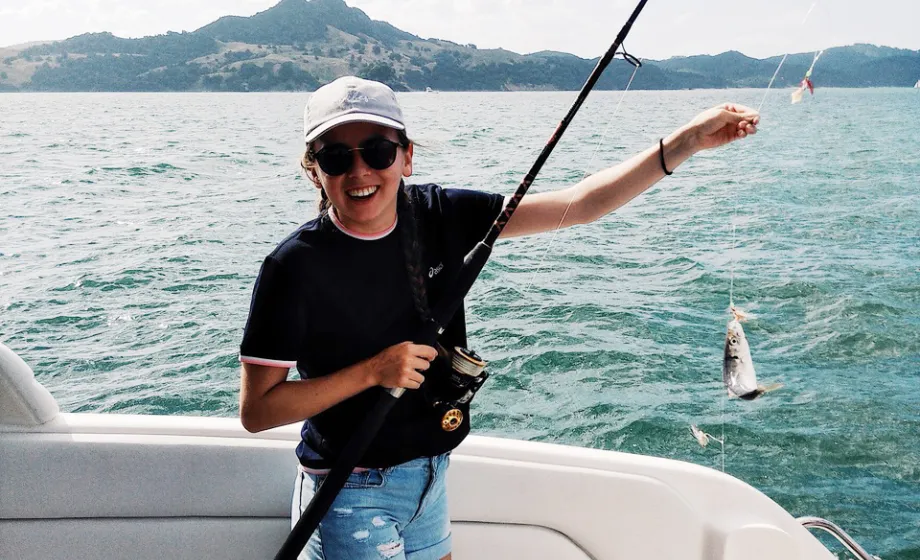 Mädchen auf Boot hält Fisch an der Angel und lacht