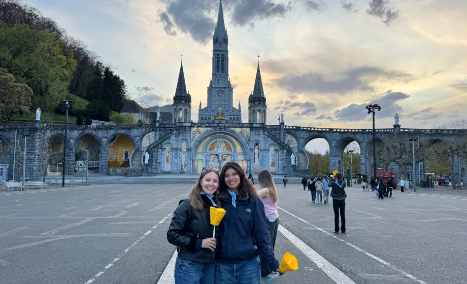 Zwei Austauschschülerinnen mit gelben Kerzen vor der Basilika in Lourdes bei Sonnenuntergang